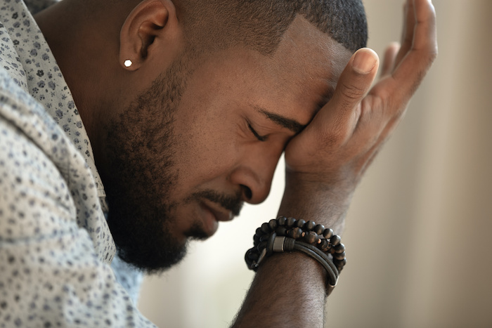 Upset stressed young african american man coping with strong headache concept, upset exhausted black guy feeling frustrated depressed tired touching forehead suffer from migraine, close up side view