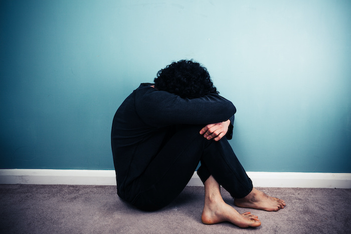 Sad young man with his head in his hands is sitting on the floor